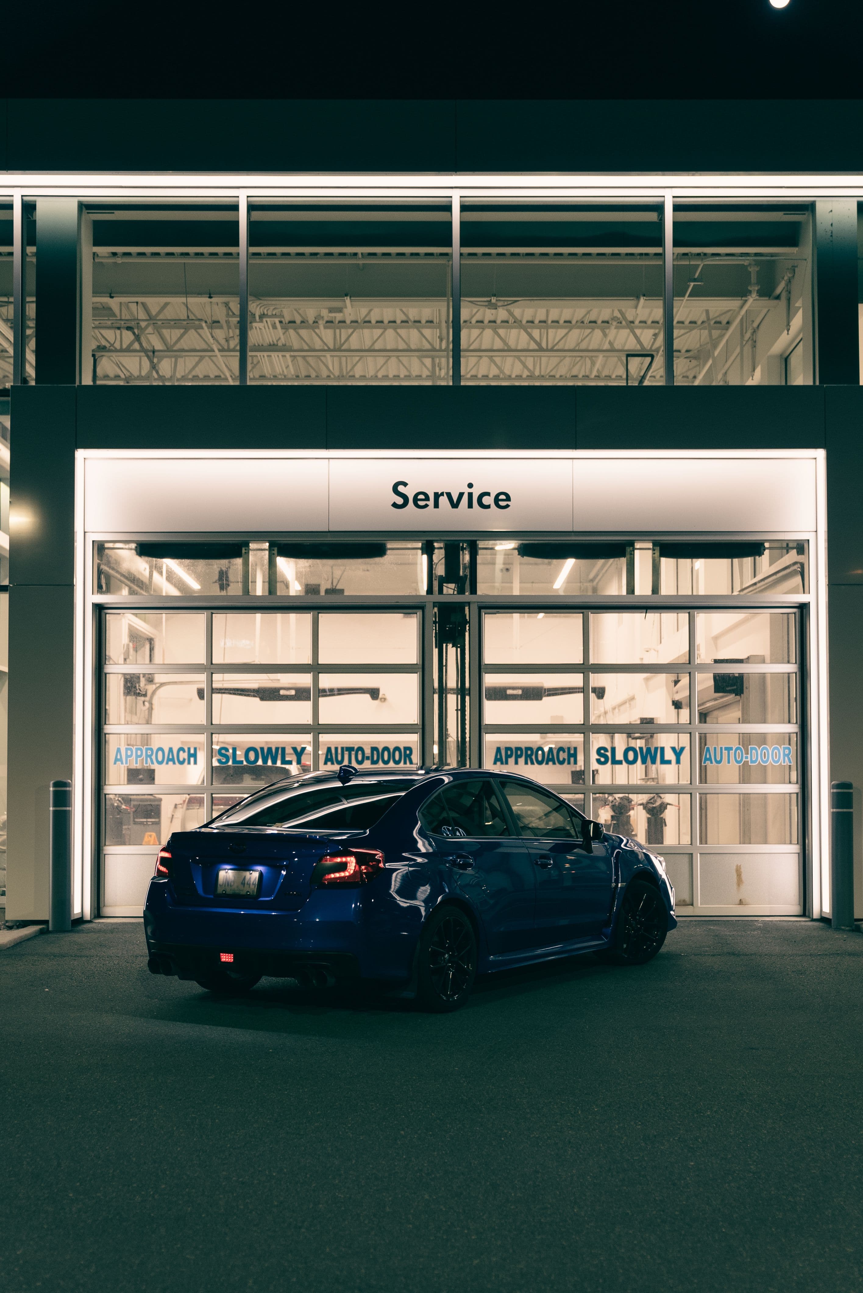 Exteriér autoservisu v noci — vůz zaparkovaný před osvětleným výjezdem servisu s nápisem Service